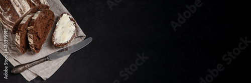 Freshly baked homemade artisan sourdough rye and white flour bread. Sliced. Bread and butter and vintage table knife on dark background. Banner. Copy space.