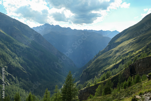 A panoramic view on vast valley with the view on Grossglockner in Heiligenblut region in Austria. The valley has lush green color. There are high Alpine chains in the back. A bit of overcast