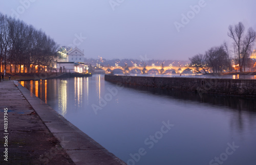 Vltava river bank after sunset and in the background blurred Charles Bridge in Prague