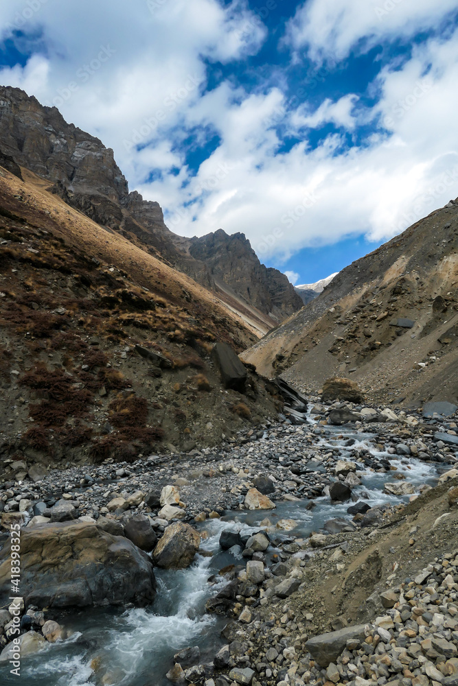 A view on rushing brook in Manang Valley, Annapurna Circus Trek, Himalayas, Nepal, with  Annapurna Chain and Gangapurna in the back. Dry and desolated landscape. High, snow capped mountain peaks.