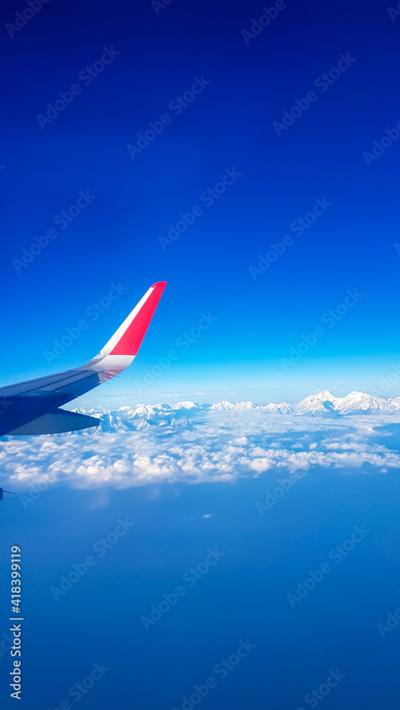 Window view from the plane on snow capped Himalayan ranges in Nepal. The high peak are shrouded in clouds. Lots of clouds below. Wing of the plane in the corner. Flying high above the ground. Freedom Window view from the plane on snow capped Himalayan ranges in Nepal. The high peak are shrouded in clouds. Lots of clouds below. Wing of the plane in the corner. Flying high above the ground. Freedom