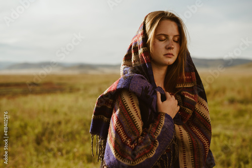 in the steppe stands a beautiful girl with a proud tired face covering her eyes wrapped in a striped ethno plaid. High quality photo