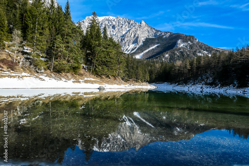 Winter landscape of Austrian Alps with Green Lake in the middle. Powder snow covering the mountains and ground. Soft reflections of Alps in calm lake's water. Winter wonderland. Serenity and calmness