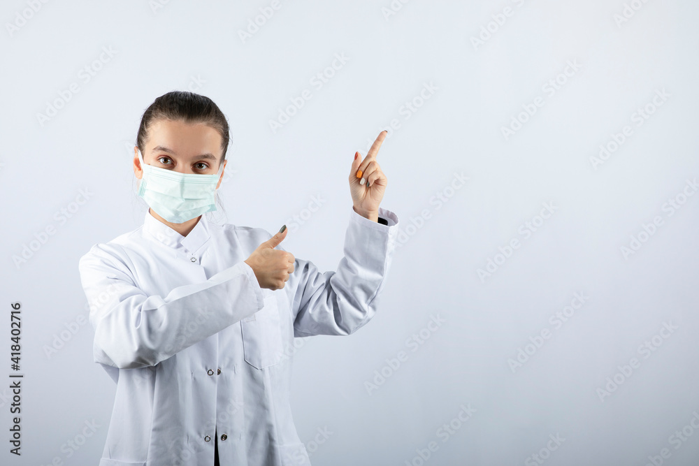 Woman doctor in white uniform wearing a medical mask and pointing away Woman doctor in white uniform wearing a medical mask and pointing away