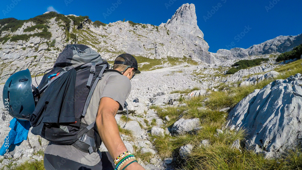 A man taking a selfie while hiking in stony Alpine region in Austria. The sky is blue, with one cloud on it. Mountains slopes barely overgrown with any bushes and grass. Summer in Alps. Exploration
