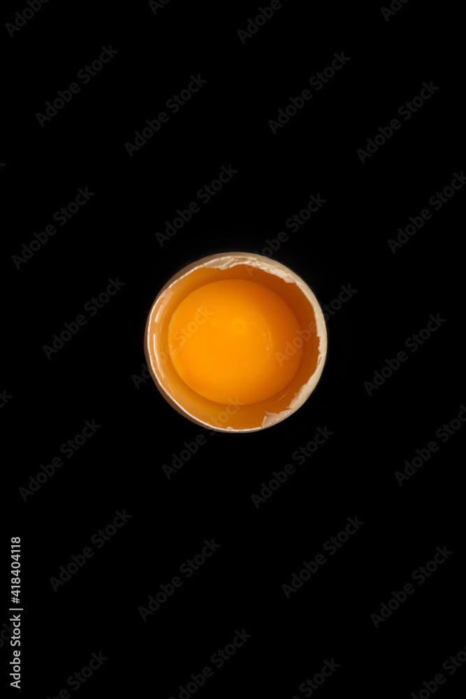 Opened egg with visible yolk in the middle on black background, minimalistic easter card