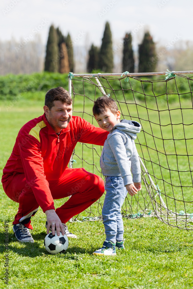 Obraz premium Father with his little son playing football, soccer in the park. Father teaches his son