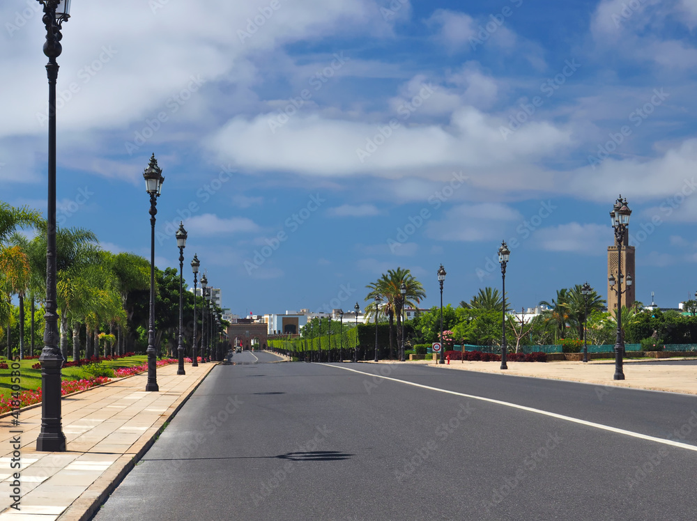 Colonial architecture and traditional building in Rabat, the capital city of Morocco. Exotic plants and palm tree avenue, flag of Morocco, clear sky blue with white clouds.