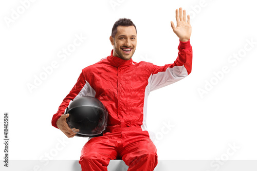 Male racer in a red uniform sitting on a panel and waving