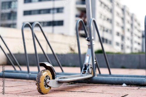 Detalle de la rueda trasera de un patinete no eléctrico estacionado en una estación de aparcamiento para bicicletas. Scooter para niños. Rueda desgastada, muy usada y rota llena de piedras.