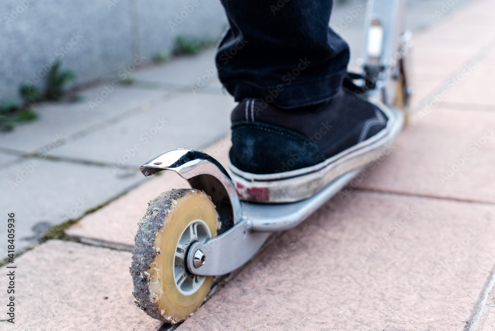 Obraz premium Detalle de la rueda trasera de un patinete eléctrico. Rueda gastada, muy usada, vieja y rota llena de pequeñas piedras.