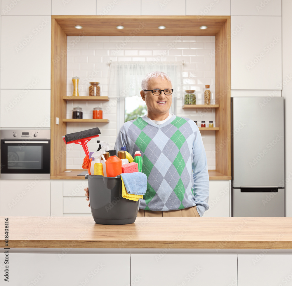 Mature man with a bucket full of cleaning supplies posing in a kitchen Mature man with a bucket full of cleaning supplies posing in a kitchen