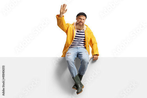 Photo Bearded fisherman with a yellow rain coat sitting on a panel and waving