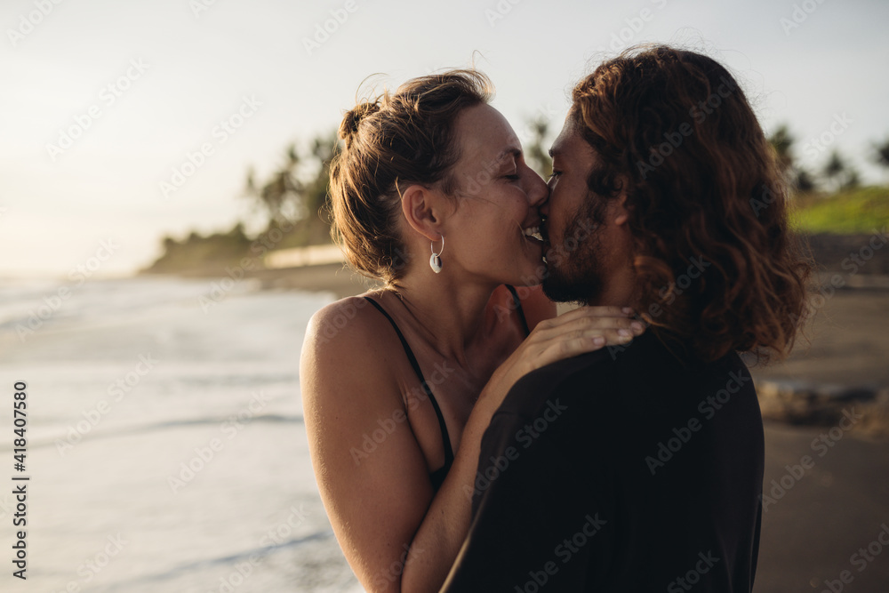 On the beach sand against the ocean, a loving couple gently embraced kissing. High quality photo On the beach sand against the ocean, a loving couple gently embraced kissing. High quality photo