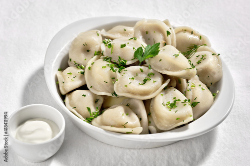 Boiled or steamed pelmeni in white bowl. Pelmeni are homemade pasta with mince meet filling wrapped in thin wheat dough. Sour cream sauce on the side.