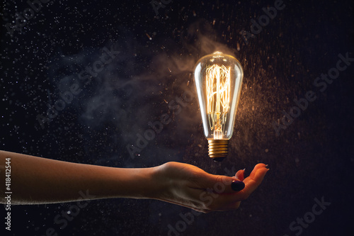 Fotografia hand holds in the air a burning vintage light bulb without wires