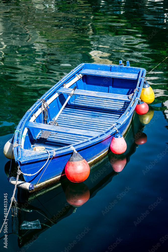 Un bote de madera azul con boyas amarillas y rojas en sus costados flota  sobre las mansas aguas de un puerto pesquero del Cantábrico español Stock  Photo | Adobe Stock