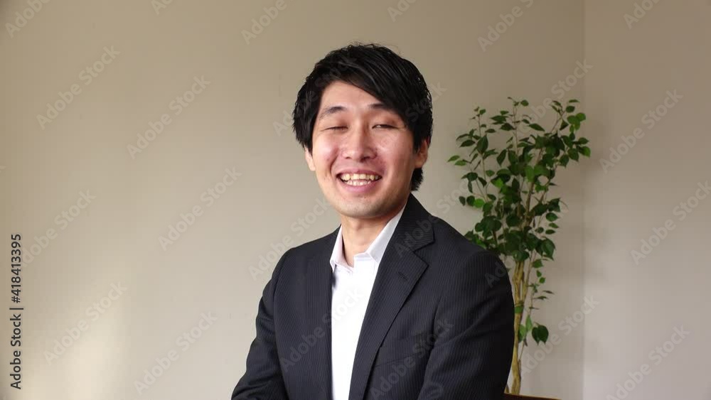 Young Asian (Japanese) business man wearing a suit at the office. One person, black hair, looking at the camera, laughing and smiling. Office worker or company employee. Job interview concept shot. Young Asian (Japanese) business man wearing a suit at the office. One person, black hair, looking at the camera, laughing and smiling. Office worker or company employee. Job interview concept shot.