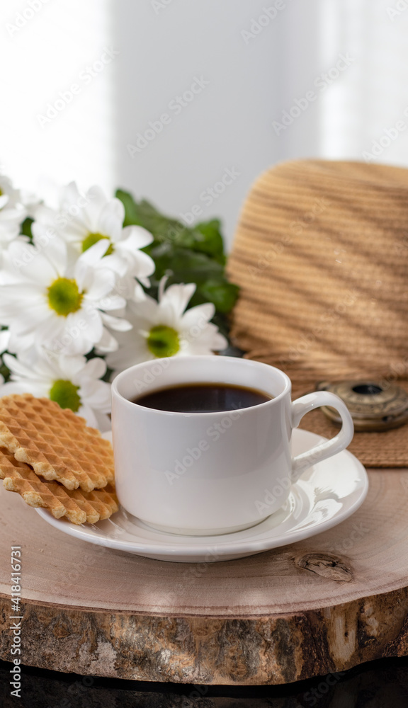 Obraz premium White cup with black coffee. Morning coffee, breakfast, cookies, tropical leaf, wicker hat. Summer sunny background. Breakfast on vacation at the hotel. Traveling at sea, close-up.