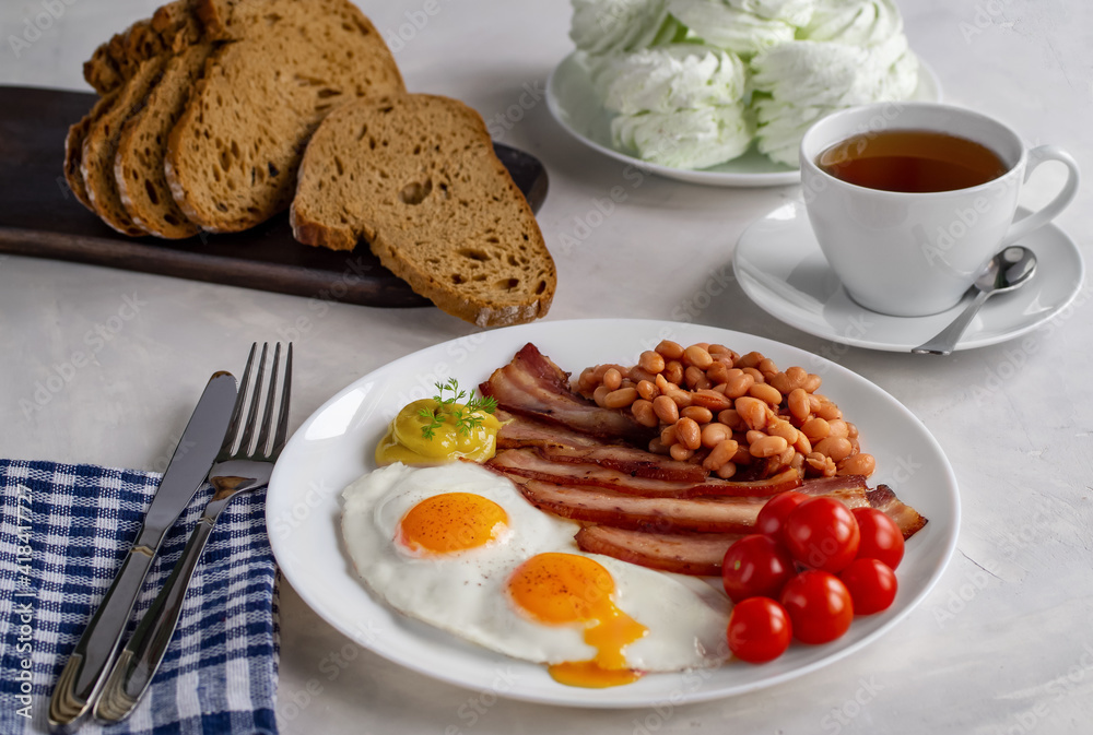 Hearty breakfast with scrambled eggs, bacon, beans, cherry tomatoes, homemade bread, tea and marshmallows on a concrete countertop. English breakfast concept. First-person view Hearty breakfast with scrambled eggs, bacon, beans, cherry tomatoes, homemade bread, tea and marshmallows on a concrete countertop. English breakfast concept. First-person view