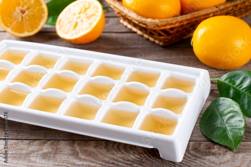 Freezing lemon juice in cubes in a tray with fresh lemons on a wooden table