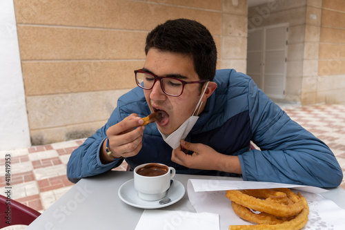 Happy young boy sitting in table and enjoying delicious churros with hot chocolate.