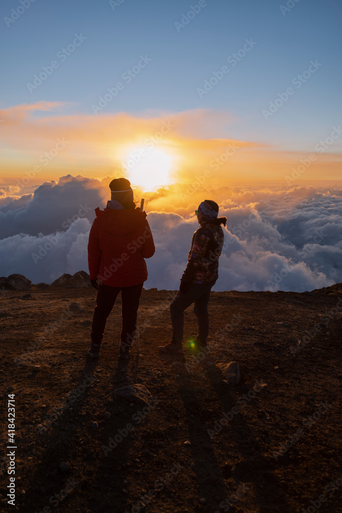 Young woman climbers on top of the Acatenango volcano in Guatemala watching the sunset - women hiking on top of the mountain while watching the sunset