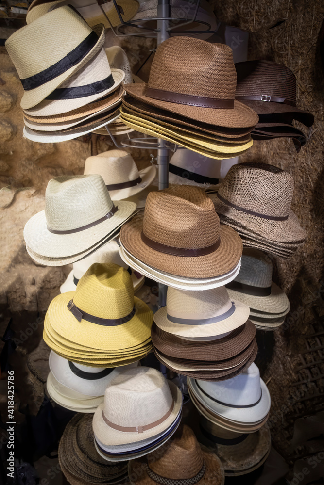 display with a multitude of cream, brown, yellow and white colored straw hats stacked one inside the other, vertical