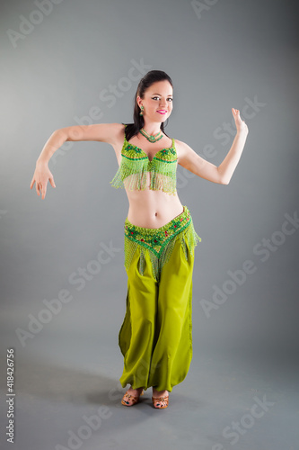 beautiful brunette girl in green belly dance costume smiles at camera in studio
