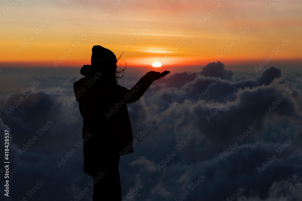Young woman on top of the mountain holding the sun with her hand during sunset-concept achievement of goals