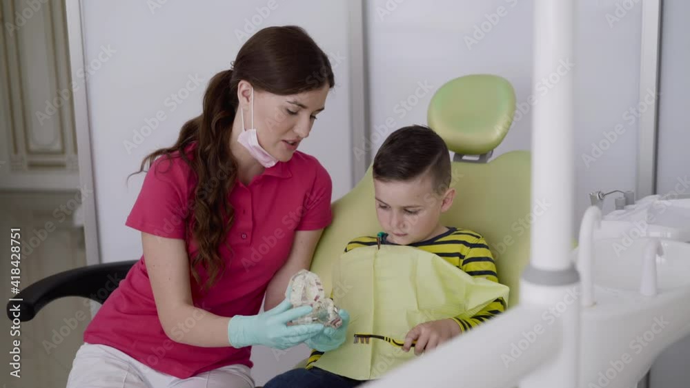 Dentist shows a boy how to brush teeth rightly using toothbrush and jaw layout Dentist shows a boy how to brush teeth rightly using toothbrush and jaw layout