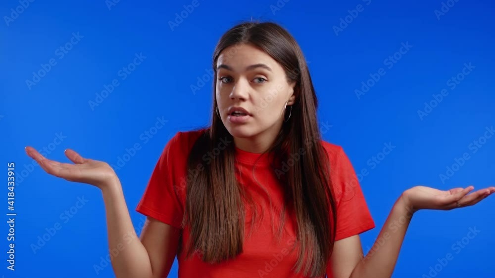 Young indifferent unsure woman makes gesture of I don't know, can't help anything. Difficult question concept. Blue studio background. Young indifferent unsure woman makes gesture of I don't know, can't help anything. Difficult question concept. Blue studio background.