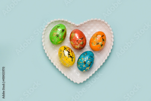 Five Easter eggs lie in a plate with a heart on a delicate background. Postcard with eggs on a light blue background. Layout for Easter. Invitation.