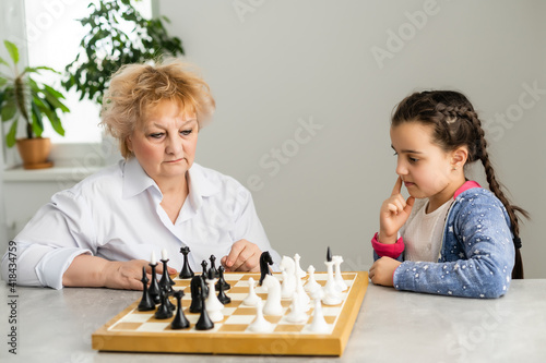 Young girl playing chess with grandmother together at home