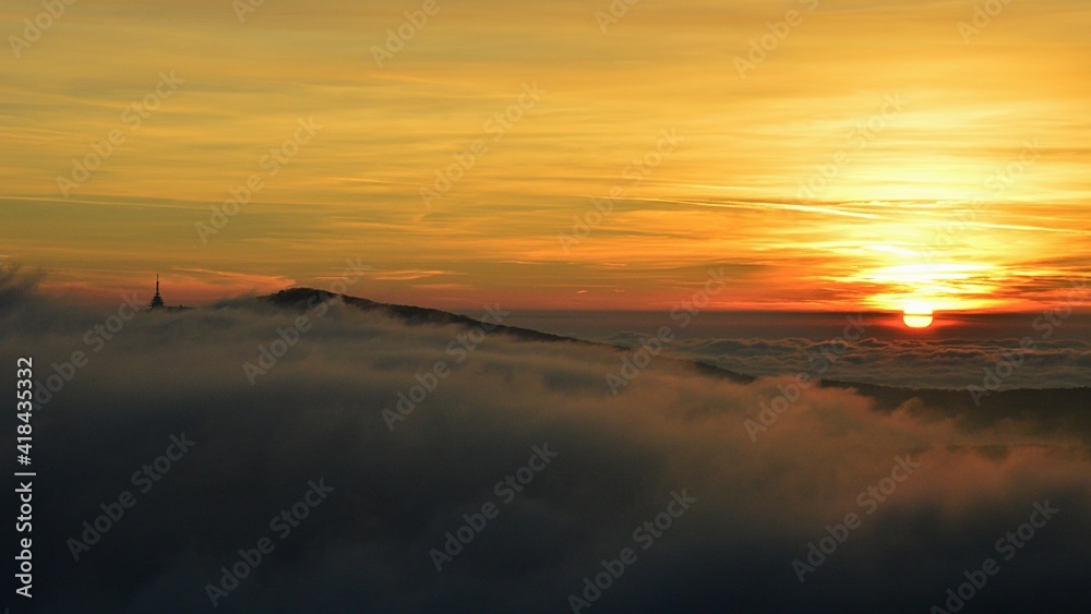 Dramatic sunset with dense fog above hills near Nitra city, western Slovakia. So called Pyramid radio tower visible on tip of Zobor hill. Dense scattered clouds on evening skies. Winter season. 