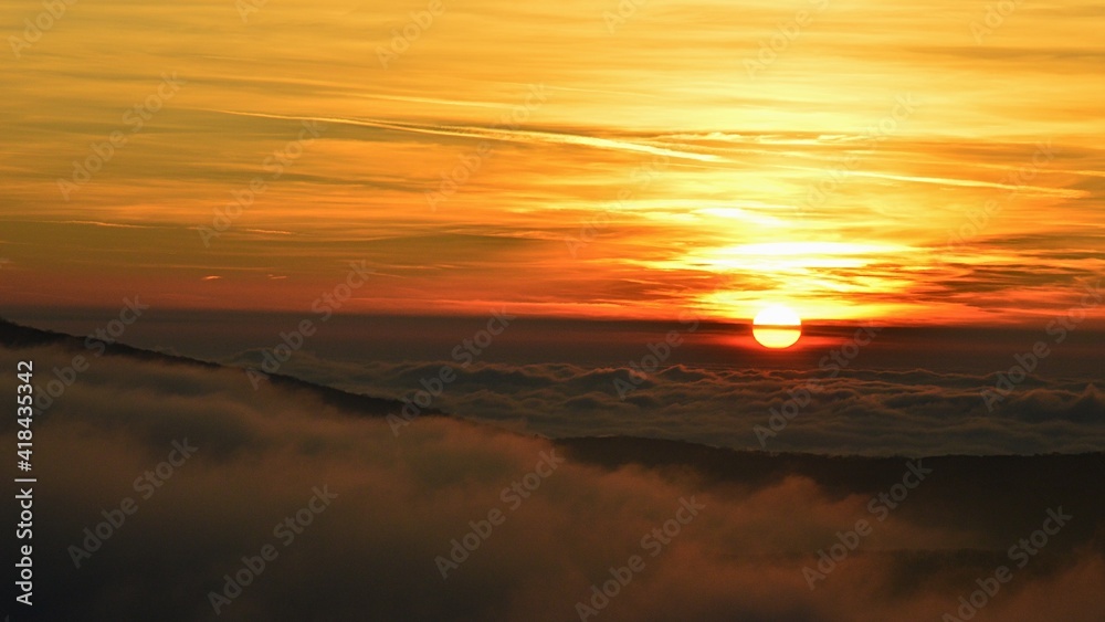 Dramatic sunset on western Slovakia uplands during late winter season, early February. Thick clumps of dense fog visible above hills tips, scattered clouds on the sky. 