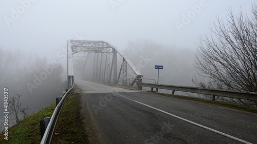 Old steel narrow road bridge above Little Danube river to Kollarovo town, western Slovakia. Sign on the bridge says Welcome To Kollarovo in Slovak and Hungarian language. Misty winter weather. photo