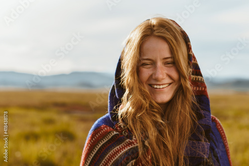 red-haired girl with a beautiful smile wrapped in plaid and stands in the steppe against the backdrop of hills. High quality photo © mnelen.com