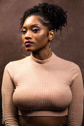 Black woman with natural hair wearing a crop top, Woman with hoop earrings and lipstick and light brown top, African American woman