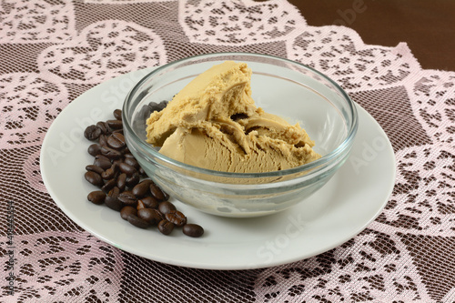 Coffee ice cream in glass bowl and coffee beans on white plate on pink heart lace table runner on brown tablecloth