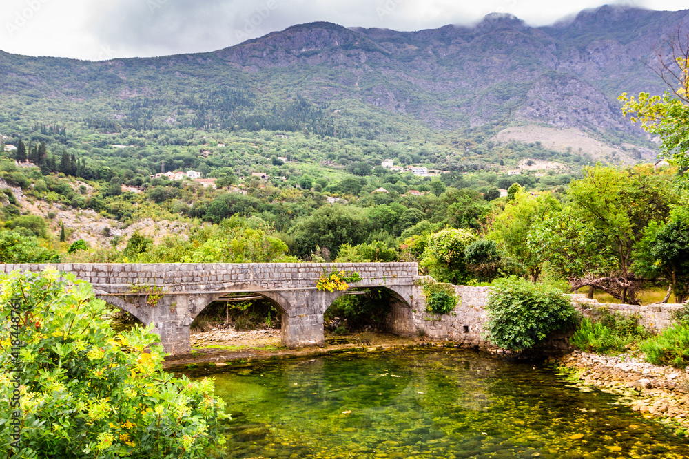 Old stone bridge over small transparent river at foot of mountains, near Risana, Boca-kotor bay, Montenegro