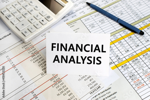 The inscription financial analysis on a white sheet that stands on a financial document on the background of a white calculator and pen. Business and financial concept