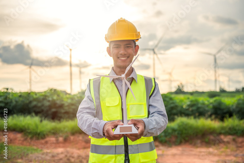 portriat of asian engineer male hand holding the wind turbine model and smiling with the background of wind turbine farm. Environmental friendly. Renewable energy technology and sustainability. 