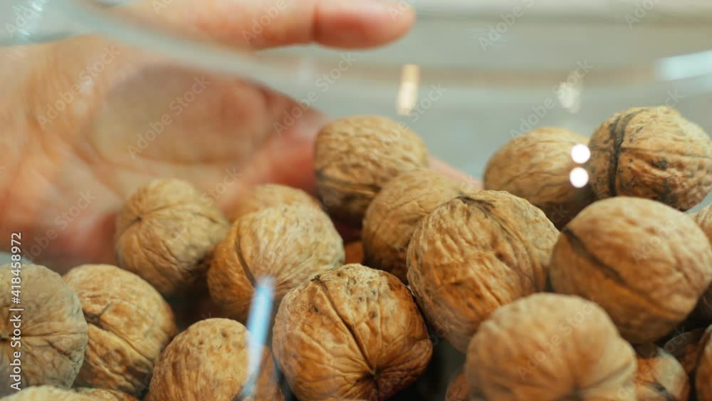 They are holding a glass container for food. It contains walnuts. The shell of the nuts is light brown in color. The capacity is set. Close-up.