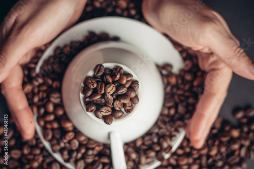 coffee beans on a saucer and an inverted white cup on a dark background female hands