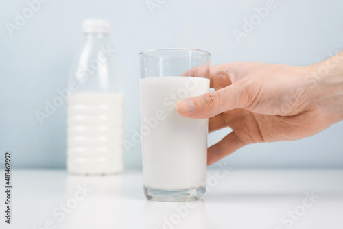 Male hand taking glass of milk in the kitchen at home. Close-up, selective focus