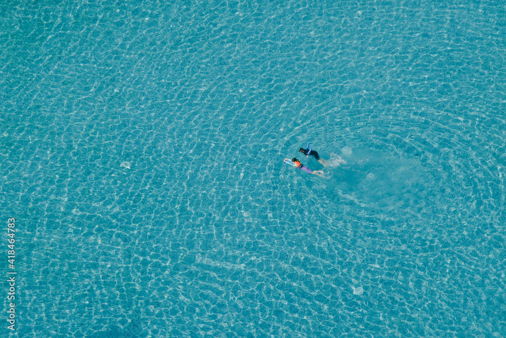 A bird's-eye view of an outdoor pool with two children swimming in the blue water as the surface rippling in the waves. A bird's-eye view of an outdoor pool with two children swimming in the blue water as the surface rippling in the waves.