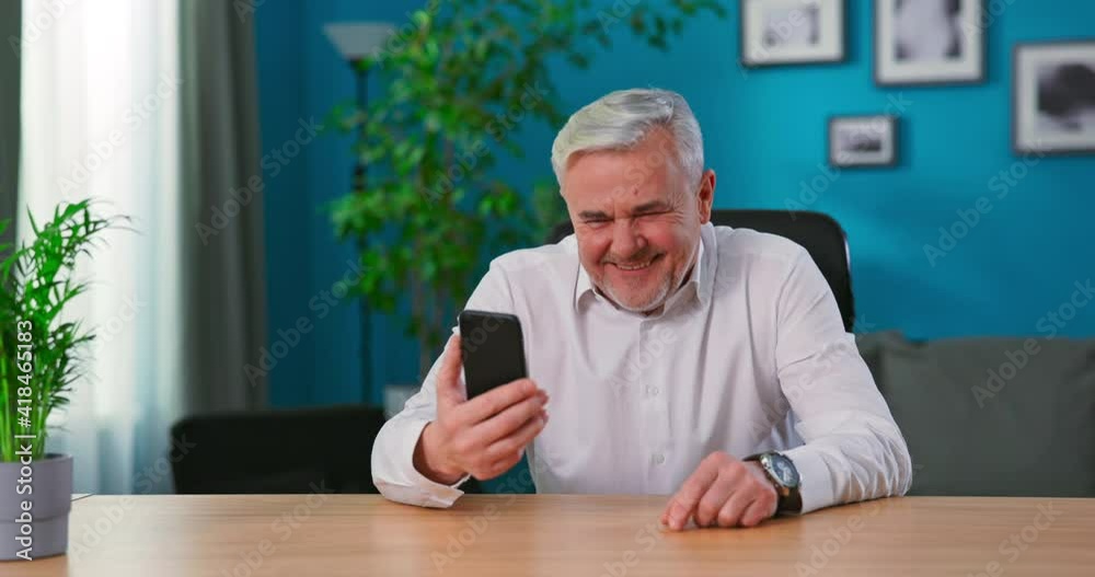 Smiling Grandfather enjoying conversation with family sharing lifestyle chatting on mobile phone. Overjoyed mature man hold phone look at screen excited about mobile app sport bet bid win concept. Smiling Grandfather enjoying conversation with family sharing lifestyle chatting on mobile phone. Overjoyed mature man hold phone look at screen excited about mobile app sport bet bid win concept.
