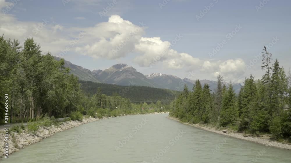 Panning shot of river amidst green trees near mountain range against sky - Golden, British Columbia