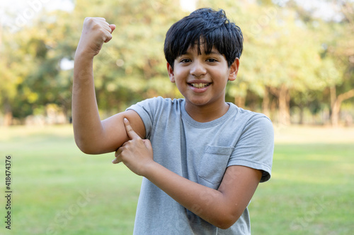 Indian boy showing muscles of the arm in the park. Concept of health